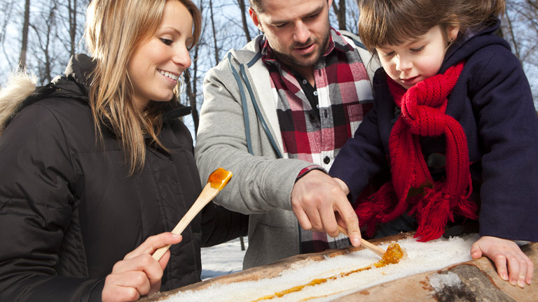 Familles homme femme avec un enfant qui mange de la tire sur neige 